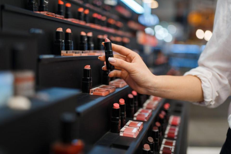  A woman picks up a lipstick from a shelf on the beauty counter.