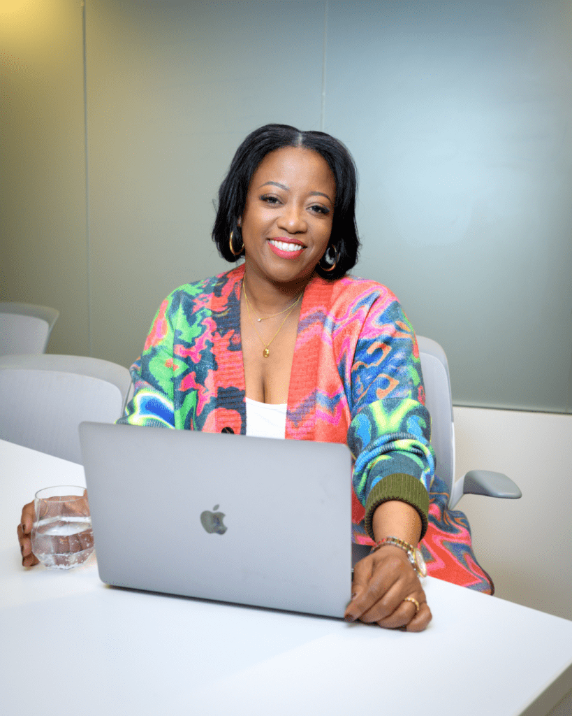 Robin Fisher smiles at the camera sitting in front of a laptop.