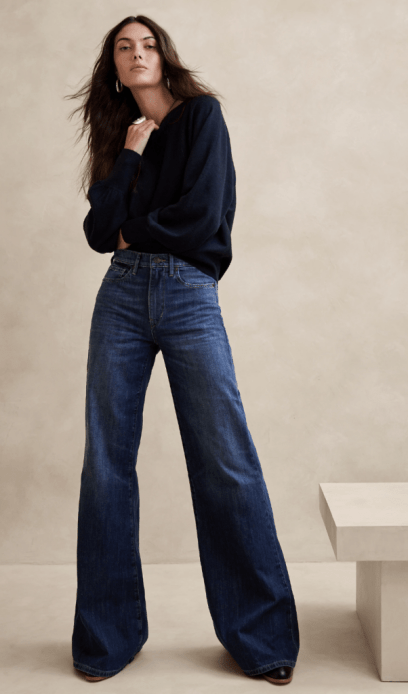 A brunette woman with long hair wears an oversized navy blue sweater and wide leg jeans.