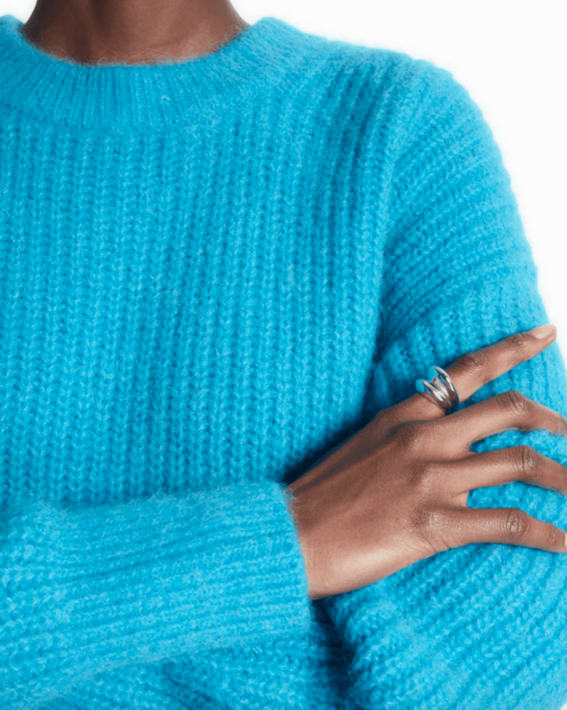 Soft cerulean sweater from the waist up, one hand on arm with a turquoise ring.